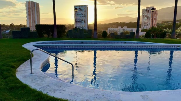Enjoy a stunning sunset view of an illuminated pool with urban buildings, creating a perfect atmosphere for relaxation