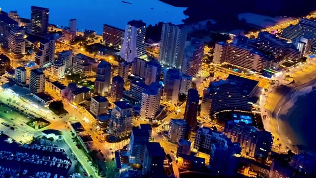 A stunning aerial view of a bustling coastal city illuminated at night, highlighting a gorgeous shoreline