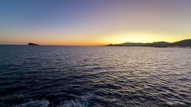 A beautiful sunset viewed over the calm ocean waters, showcasing vibrant colors and a scenic coastline.