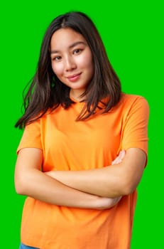 A young woman with straight, dark hair stands confidently with her arms crossed, wearing an orange shirt. The vibrant green background adds energy to the composition.