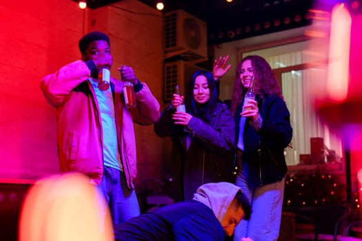A group of friends celebrates together, clinking their drinks and dancing joyfully in a warm, inviting indoor space illuminated by colorful lights. The atmosphere radiates fun and camaraderie.