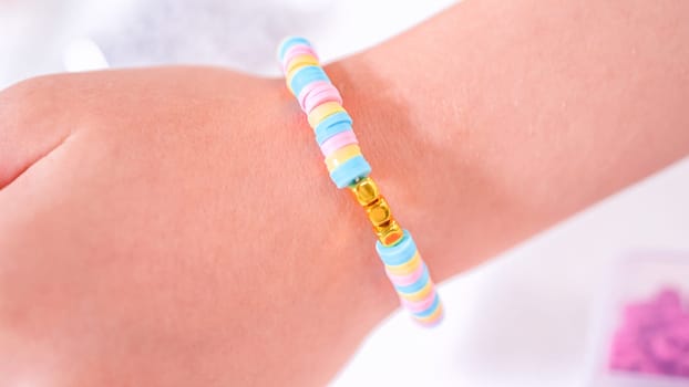 Delicate fingers of a young girl navigate through a treasure trove of bright, multicolored beads, each compartment revealing a new hue to choose from. She's immersed in the joyful task of stringing together a handmade bracelet, with golden beads and pearls lying nearby to add a touch of sparkle to her creation.