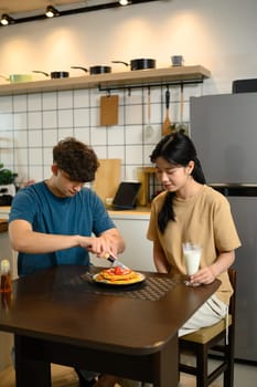 Young couple enjoying a homemade breakfast together with pancakes and a glass of milk.