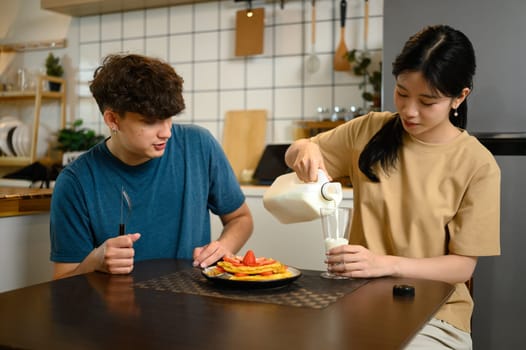 Young couple enjoying a homemade breakfast together with pancakes and a glass of milk.