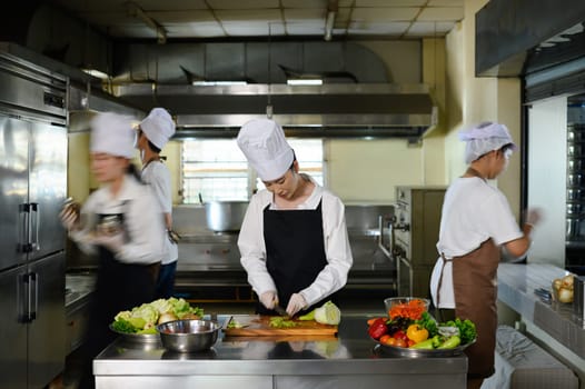 Busy cooking class in session with multiple students in uniforms preparing fresh ingredients.