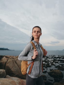 Confident woman in athletic outfit standing on a rocky beach, symbolizing adventure and an active lifestyle, surrounded by beautiful seascape and cloudy sky