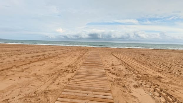 A tranquil and serene beach pathway made of beautiful wooden planks stretches against a calming ocean backdrop
