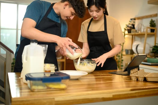 Man pouring milk into a bowl while preparing pancake batter in the kitchen.