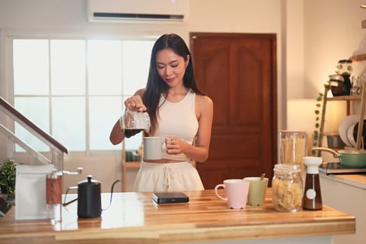 Charming Asian woman preparing her daily cup of coffee in a relaxed kitchen.