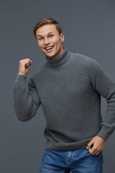 happy young caucasian man wear gray knitted sweater smiling cheerfully show fist gesture express success and motivation isolated on dark background. Positive emotion with mental health and digital detox theme. Concept: mental wellbeing