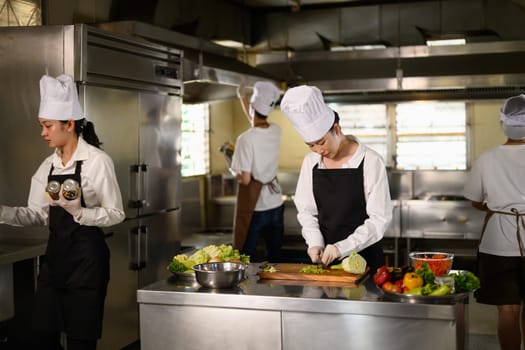 Busy cooking class in session with multiple students in uniforms preparing fresh ingredients.