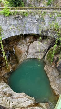 Natural pool in Italian Orrido di Bellano near lake Como surrounded by rocky cliffs and lush greenery beneath a stone bridge, featuring tranquil water and a vibrant nature scene