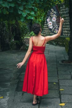 back of a woman in a red dress with a beautiful fan in a garden in Asia. Travel and tourism in Asia