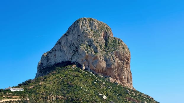 A breathtaking view of an enormous rock formation gracefully surrounded by lush, vibrant greenery and clear blue skies