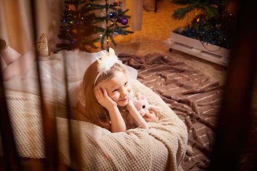 A joyful child relaxes on a blanket while admiring Christmas decorations and gifts, surrounded by festive lights.