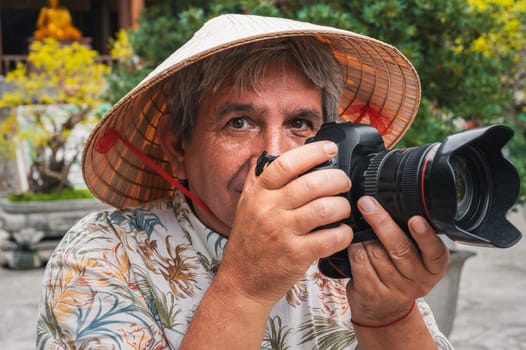 elderly man travel photographer in a Vietnamese hat takes pictures with camera at pagoda in Nha Trang in Vietnam. Tourism and travel in Asia