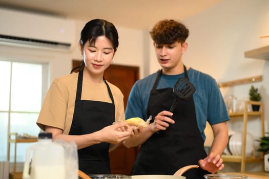 Happy young couple cooking pancakes together in a warm kitchen.