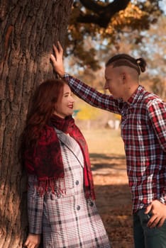 young couple in love hugging in autumn park. they look at each other lovingly. girl in coat, against the background of autumn trees, golden autumn around