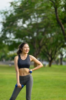 Smiling young woman exercising with dumbbells in the park. Health and fitness concept.