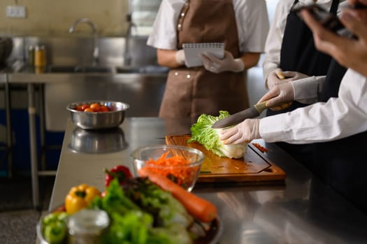 Chef guiding students in vegetable preparation during a hands-on culinary class.