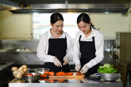 Chef instructor guiding a student on proper vegetable cutting techniques in a kitchen.