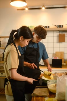 Happy young couple cooking pancakes together in a warm kitchen.