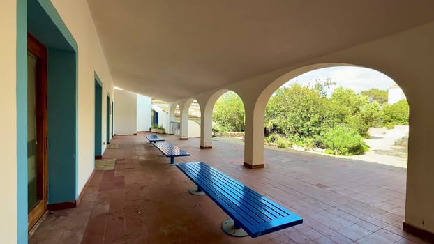 This outdoor corridor offers a serene escape with blue benches and elegant architecture, surrounded by lush greenery