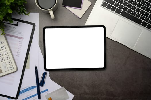 Top view of digital tablet with blank, financial reports, and laptop on stone desk.