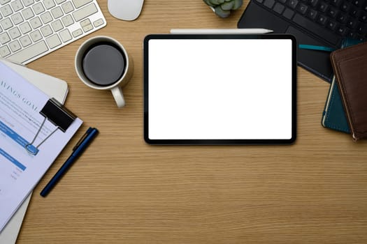 Digital tablet with blank screen on office desk surrounded by coffee, stationery and documents.