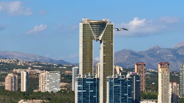 A unique perspective showcasing a modern highrise building within an urban landscape, framed by majestic mountains