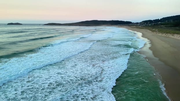 A breathtaking and stunning aerial capture that beautifully showcases tranquil ocean waves beneath a pastel sunset sky