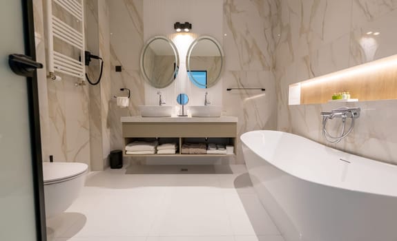 A modern hotel bathroom with freestanding bathtub, double sink, toilet and round mirrors in elegant