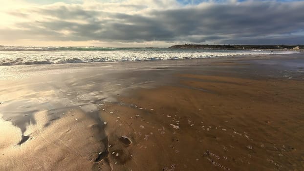 A tranquil beach view displays gentle waves lapping on warm sand beneath a dramatically cloudy sky above