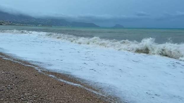 A truly beautiful beach scene showcasing waves crashing powerfully on the pebbled shore beneath a moody sky