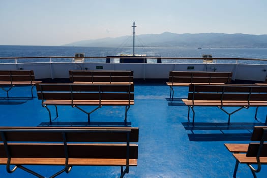 Sicily, Italy - 27.07.2024: Empty deck with benches on ferry overlooking sunny coastal landscape.