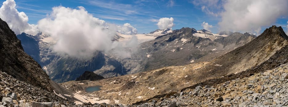 A stunning panoramic view of a majestic mountain range with glaciers, rocky terrain, and clouds rolling over the peaks, capturing the dramatic beauty of high-altitude landscapes