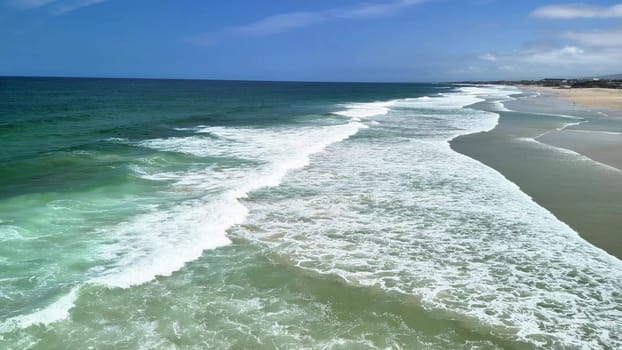 Majestic ocean waves gracefully roll onto a stunning, beautiful sandy beach beneath a bright blue cloudless sky