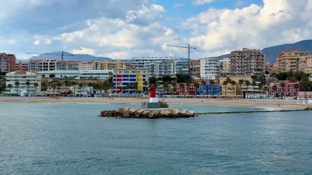 A picturesque coastal view featuring a historic lighthouse and vibrant city buildings near the sandy beach