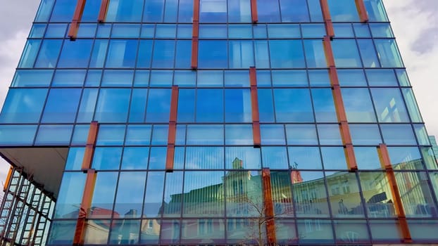 A striking modern glass building is reflecting the surrounding architecture found in a bustling urban environment
