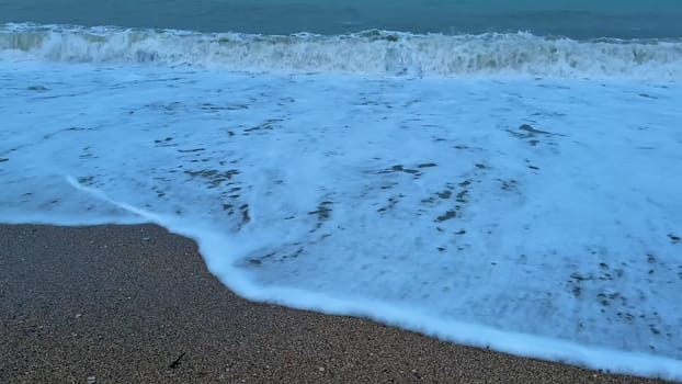 The peaceful ocean waves gently wash over the sandy beach as the sun sets under a beautiful dusk sky