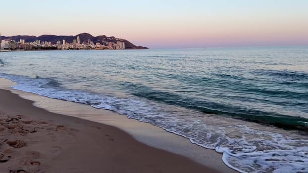A serene beach at sunset, with gentle waves lapping the shore and a breathtaking skyline on the horizon