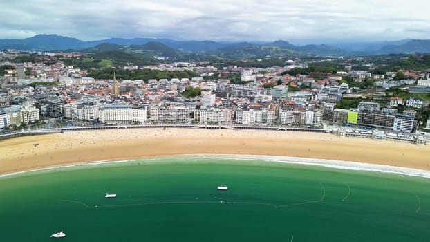 A stunning aerial shot beautifully depicts a picturesque beach nestled next to a lively, vibrant coastal town