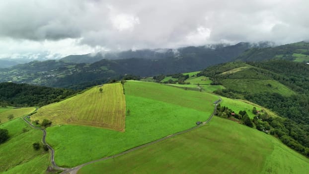 The stunning drone footage beautifully showcases the vibrant green fields and majestic mountains beneath a cloudy sky