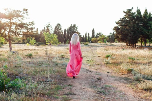 Blonde woman in pink dress walking at sunset in park