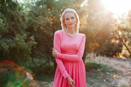 Blonde woman in pink dress smiling at sunset