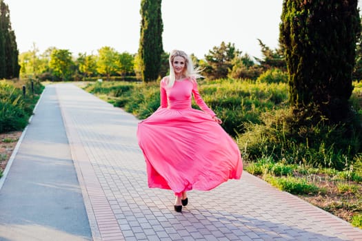 Blonde woman in pink dress walking at sunset in park