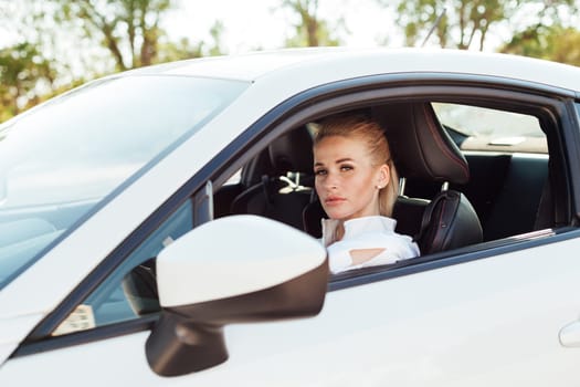 Woman blonde driver driving a white sports car on the road