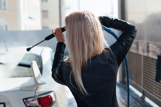 Woman washing car with foam and water at car wash