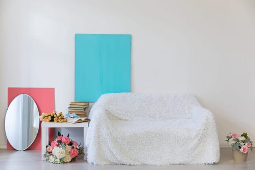 White sofa with flower vases in the interior of a white room with a window