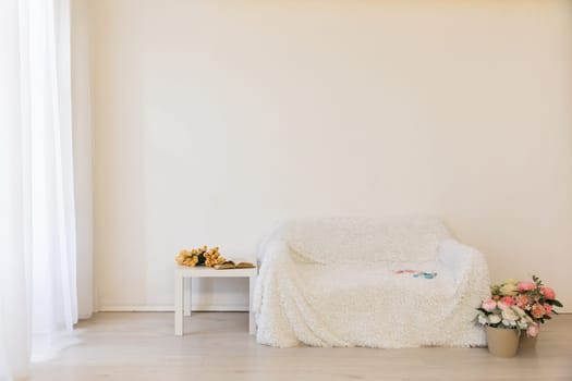 White sofa with flower vases in the interior of a white room with a window